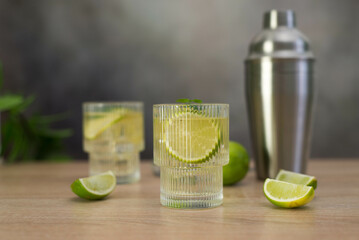 two fresh cold glasses of mahito with lime and shaker on a gray-green background.