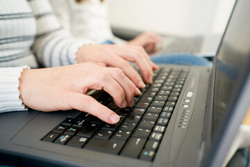Side view of anonymous woman in casual clothes typing on laptop keyboard while working on freelance work at home