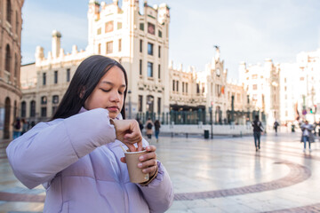 Girl with paper chocolate cup in the city centre dipping something. Concept of churros street food...