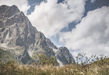 Sunny landscape in the mountains with a rocky vertical peak against a cloudy sky, mountain summer landscape