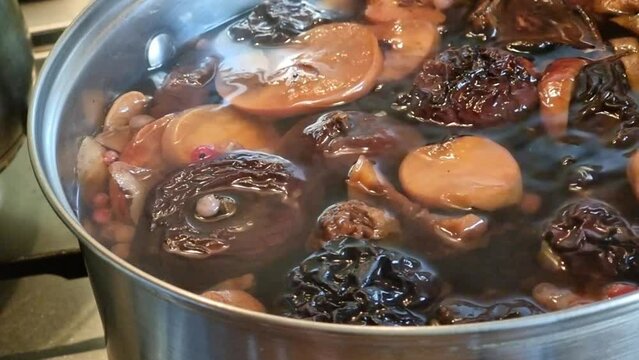 Preparation of dried fruit compote in a saucepan. Slow bubbling of boiling water and red currant berries, dried apples and pears. Stewed fruit.
