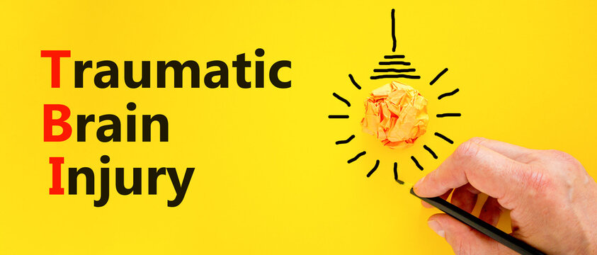 TBI traumatic brain injury symbol. Concept words TBI traumatic brain injury on paper on beautiful yellow background. Orange light bulb icon. Medical and TBI traumatic brain injury concept. Copy space.