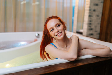 Portrait of charming young woman relaxed sitting in bath tub with hydromassage at luxury spa salon,...