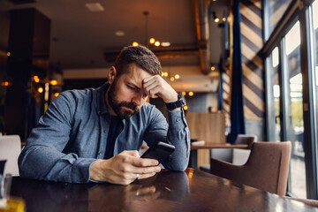 A depressed man is sitting in cafe at the table and desperately waiting for the meeting while...