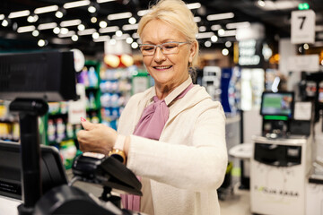 Fototapeta na wymiar A happy senior woman is paying with smart watch on self-service cash register at the supermarket.