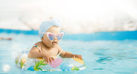Cute funny toddler girl in colorful swimsuit and sunglasses relaxing on inflatable toy ring floating in pool have fun during summer vacation in tropical resort. Child having fun in swimming pool. 