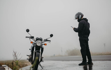 Motorcycle breakdown in the rain road, motorcyclist with smartphone.