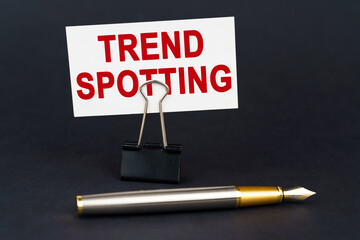 On the black surface is a pen, an office paper clip with a business card on which is written -...