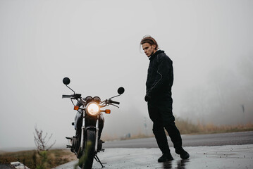 man in motorcycle clothes stands on the road near a motorcycle with rain and fog cold. Motorcycle...