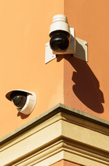 Surveillance cameras are installed on the orange wall of the building.