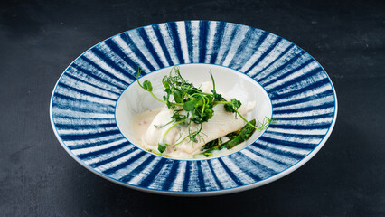 Baked halibut fish fillet with asparagus, milk sauce and microgreens.