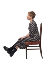  side view portrait of a woman in dress and boots sitting on chair and on white background