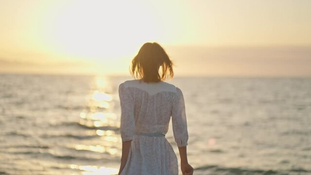 Silhouette of carefree woman with open arms standing at beach, enjoying orange sundown over the ocean. Girl silhouette at sunset
