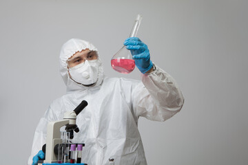 Scientific virologist. Biologist in protective suit and blue gloves holds flask with substance sample. Flask with viruses concept. Medicine and antidote in doctor hands. Virus University employee.