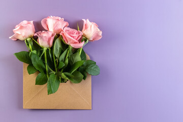 Pink roses in a paper envelope on a on a violet background. Creative gift. Flat lay. Copy space. Photo