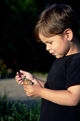 A little boy is holding a big snail in his hand.