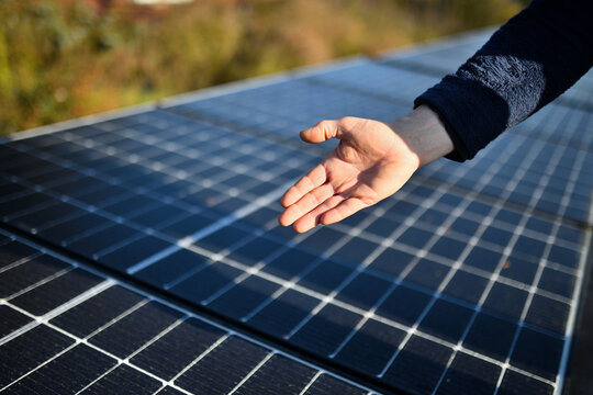 Nahaufnahme einer Hand eines Solar Installateurs mit neuen Fotovoltaik Modulen im Hintergrund auf dem Haus Dach
