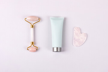 Pink jade roller and gua sha for face massage with cream or gel for the face. Facial massager tools. Anti age, lifting and toning care. Modern selfcare concept. Flat lay style.