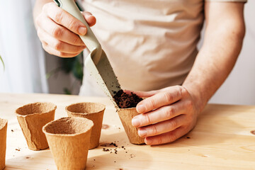 A man is sowing seeds in ecological peat cups. A man is shoveling soil for planting. Gardening as a...