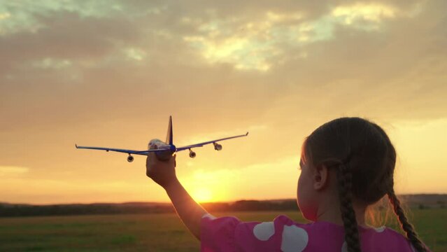 Happy girl runs with toy airplane on field in sunset light. Child play toy airplane. Kid aviator dreams of flying and becoming pilot. Little girl child wants to become pilot and astronaut. Slow motion