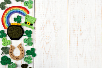 St Patrick's Day concept. Knitted composition of a green hat, a pot of gold, a horseshoe, a rainbow and green shamrocks on a white wooden background. Copy space, flat lay