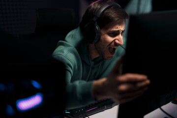 Cybersport gamer in headset touching computer monitor while celebrating successful game in dark room