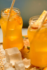 two mason jars filled with orange juice and ice cubes on a wooden cutting board