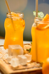 two mason jars filled with orange juice and ice cubes on a wooden cutting board