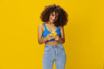 Influencer woman with phone in hand taking selfies talking on video call freelancer social media technology work, with curly afro hair in blue shirt yellow background , smile with teeth, copy space