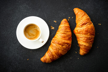 Croissant and cup of coffee at black background. French pastry, bakery, breakfast. Top view.