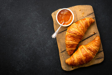 Croissant with jam on cutting board at stone table top view. Traditional dessert or breakfast.