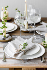 Rustic zero waste wedding decor with natural elements. Wooden table, candles, linen napkins, branches with green leaves. Eco-friendly decoration for the special dinner. Romantic and cozy place