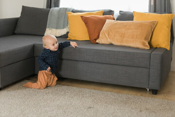 Caucasian baby newborn infant making first steps. Cute toddler kid child son boy learning walking creeping on living room copy space. Childcare and childhood concept