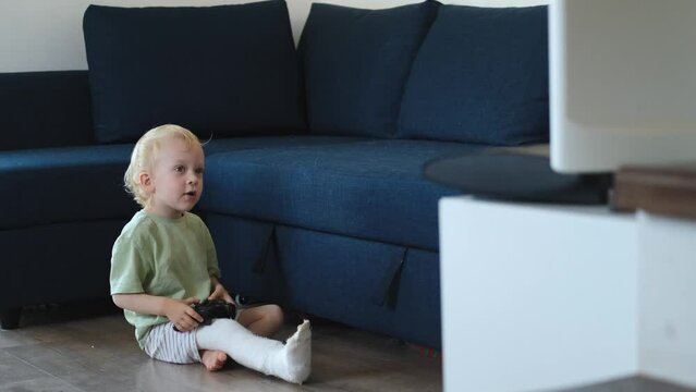 the boy sits on the floor in front of the TV and plays the console