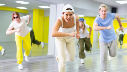 Fototapeta premium Group of expressive young teenage dancers in casual clothes exercising dance together in modern gym studio