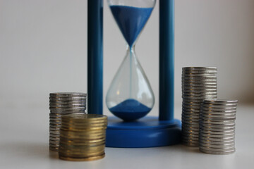 Time is Money. Coins in columns surround an hourglass with sand falling down