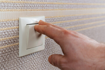 men's hand on White light switch on the wall with brown wallpaper. 