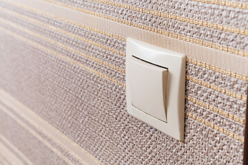 White light switch on the wall with brown wallpaper. 