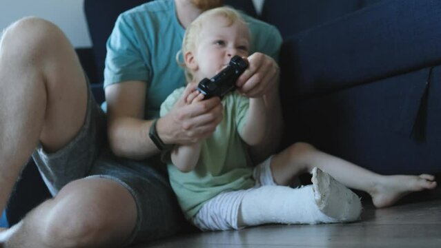 close-up father and son with a bandaged leg playing console sitting on the floor