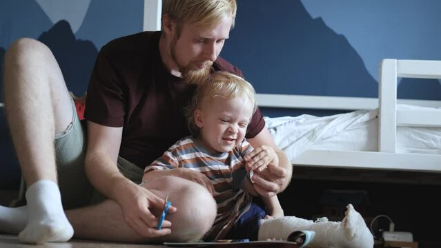 father and son gluing stickers into an album while sitting in a children's room
