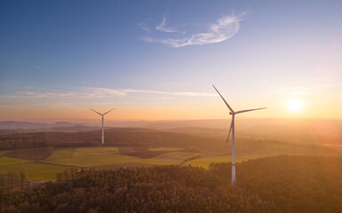 aerial view of wind turbines over forest and fields and under the blue sky at sunset
