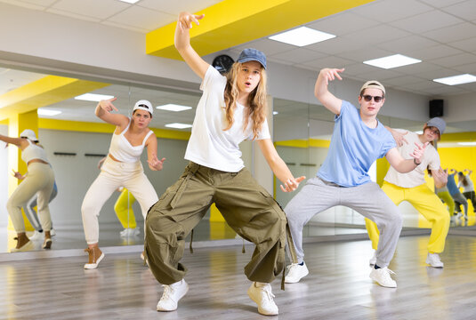 Active teenage girl with cap practicing breakdance Toprock moves in training hall. Teenagers engaged in breakdance