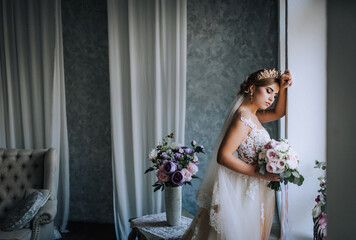 A beautiful young blonde princess bride in a white lace dress with a crown, diadem stands in the...
