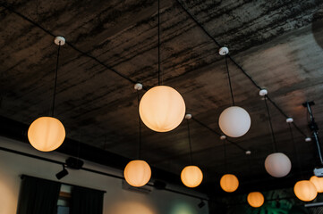 Large luminous round pendant lamps, chandeliers hang indoors on the ceiling in the interior of the house, restaurant. Photo, close-up.