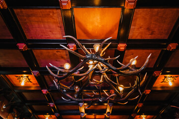 Deer antlers, a chandelier with lamps, hanging on the ceiling in the interior of the restaurant, room. Photography, decor, killing an animal.