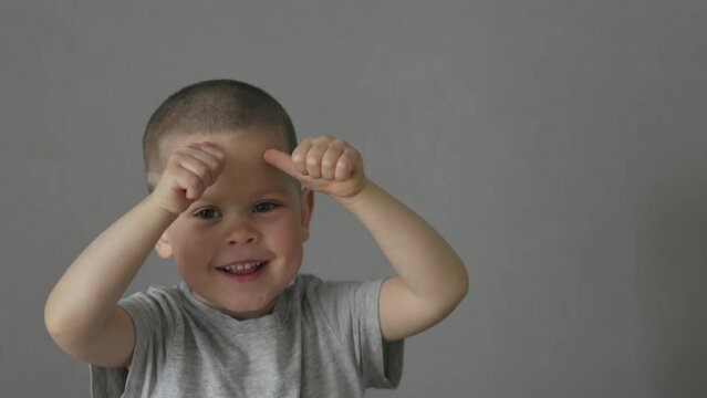 happy laughing child boy showing two fists thumb up on camera. male kid preschooler making face show satisfied sign success gesture concept happy life double thumb up. boy 4 years old grey t-shirt