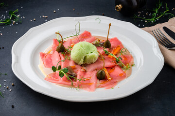 Cold appetizer of salmon carpaccio with anchovies, capers, sherbet, sauce and microgreens.