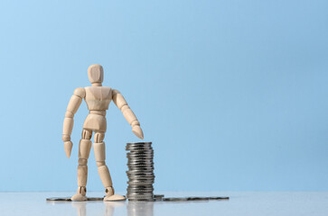 Wooden mannequin and a stack of coins on a blue background