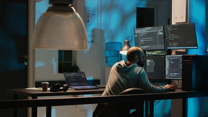 IT system engineer coding interface on multiple monitors to program new server system late at...