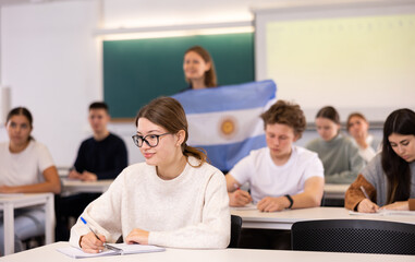 Geography lesson in school class - teacher talks about Argentina, holding a flag in his hands